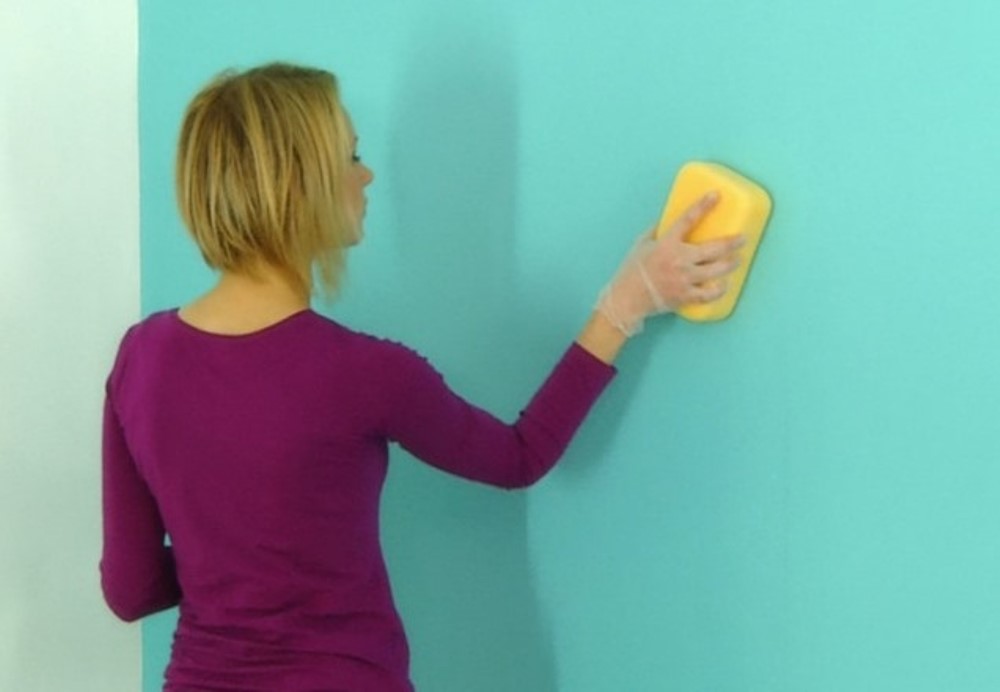 Femme lavant un mur bleu avec une eponge