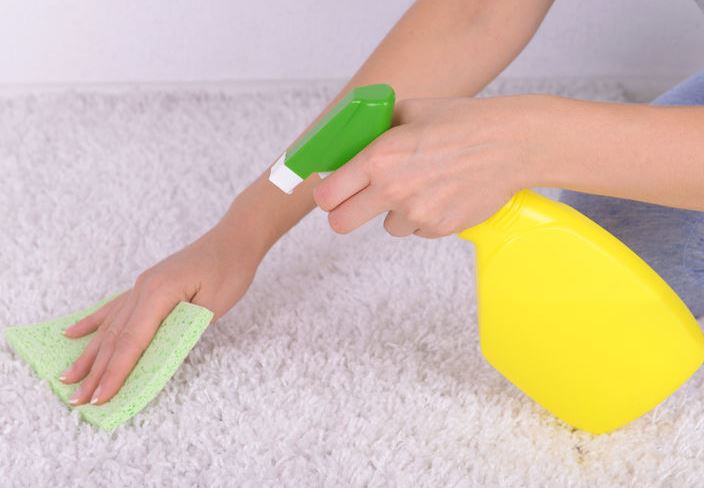 Main féminine nettoyant un tapis blanc avec un vaporisateur et une eponge