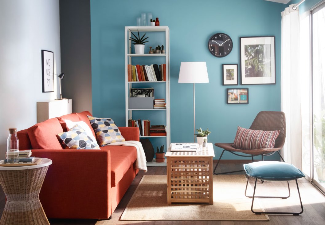 Salon avec un mur bleu, un canapé orange et table basse en bois